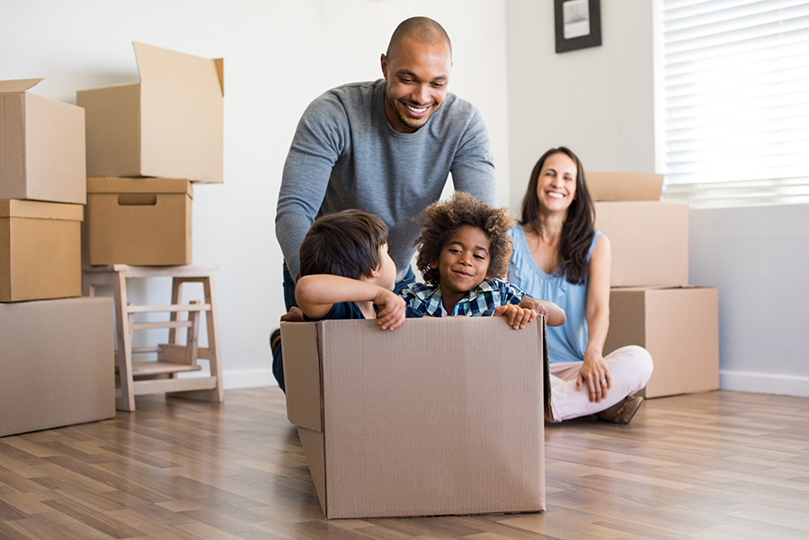Two kids playing in a cardboard box on the floor while a father and mother smile