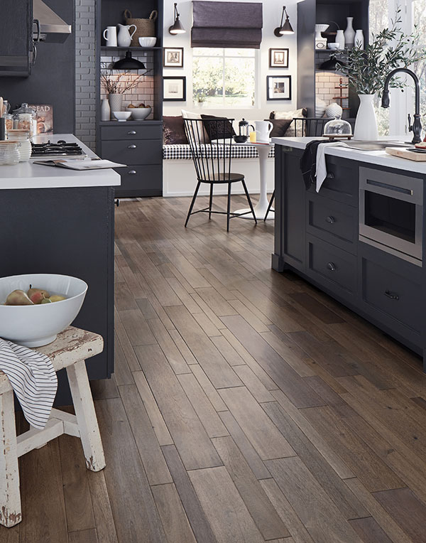 A kitchen with grey cabinets, white countertops and trendy wood floors that are a mix of wide and thin planks.