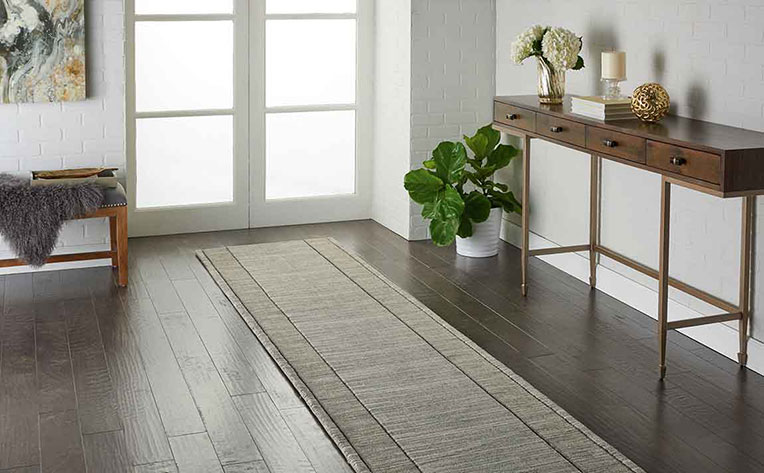 Home entryway with white brick walls, potted green house plant, runner area rug on engineered wood flooring.